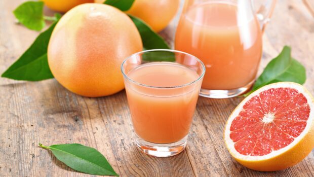 Fresh grapefruit juice with whole and halved grapefruits on wooden table
