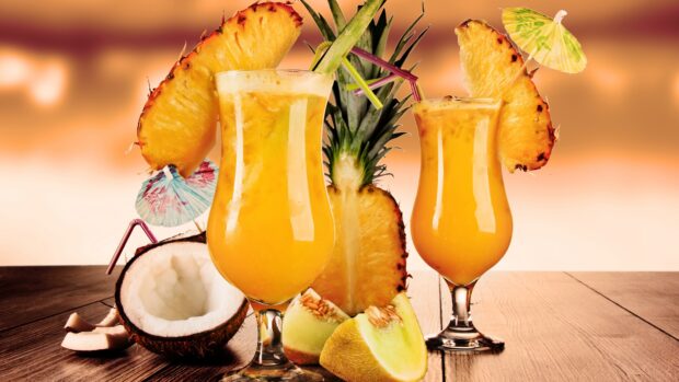 Two tropical juice drinks with pineapple slices and melon pieces on wooden table