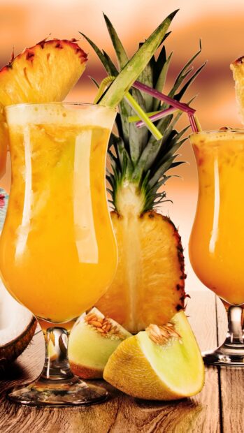 A refreshing juice with pineapple and melon slices on a wooden table in a tropical setting
