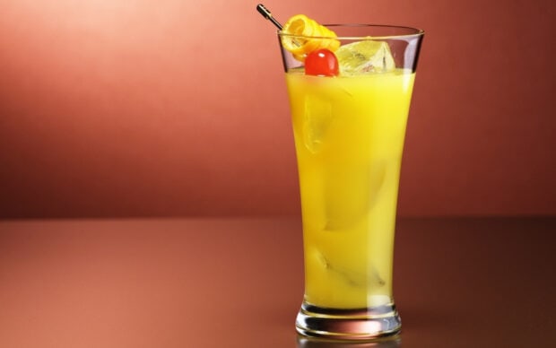 A refreshing glass of citrus juice garnished with a cherry and lemon slice on a brown surface