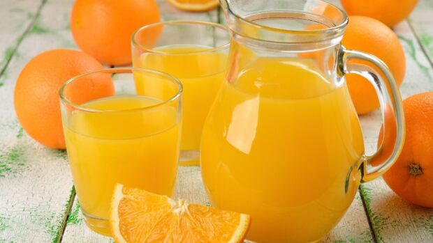 Fresh orange juice in a glass pitcher with glasses and ripe oranges on a wooden table
