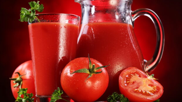 Fresh tomato juice with ripe tomatoes and parsley in a glass and pitcher on a red background