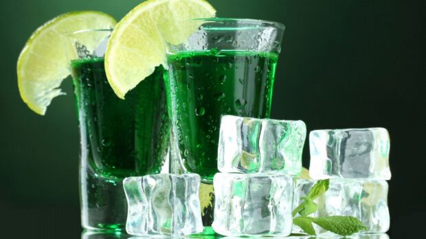 Green juice with lemon slices and ice cubes on a dark background