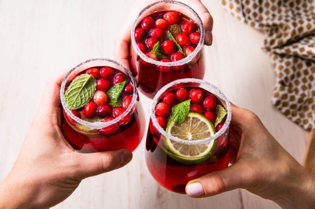 Hands holding glasses of fresh juice with cranberries and mint leaves