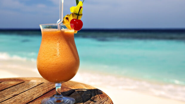 A tropical juice drink garnished with cherry and pineapple slice on the beach table