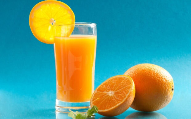 A fresh orange beside a glass of orange juice with a slice of orange on the rim