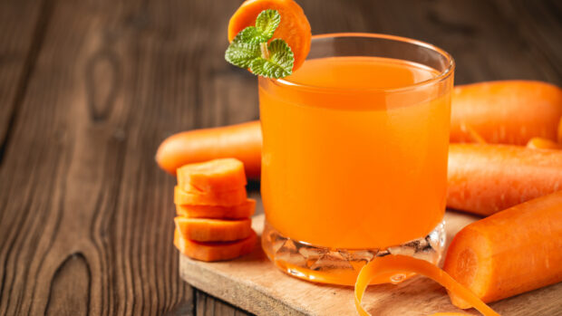 Fresh carrot juice with carrot slices and mint on wooden board