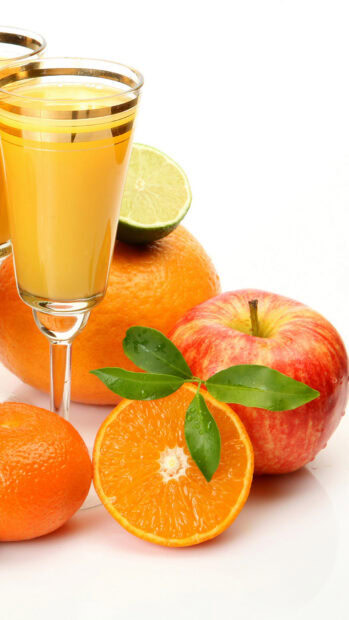 A glass of fresh juice surrounded by citrus fruits and an apple with green leaves