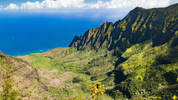 A stunning Kauai ridge with lush green valleys and deep blue ocean under a partly cloudy sky