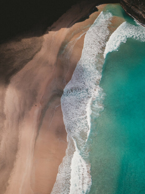 Aerial view of Kauai waves crashing on sandy shore with clear turquoise water