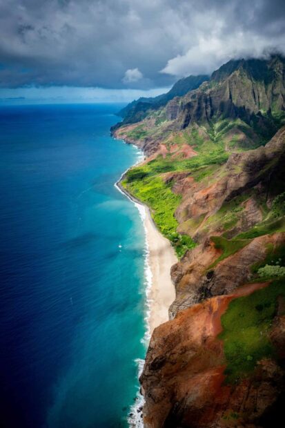 Dramatic Kauai coastline with lush greenery and cliffs under cloudy sky