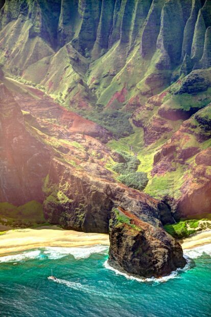Lush Kauai cliffs and beach with sailboat on turquoise ocean waters