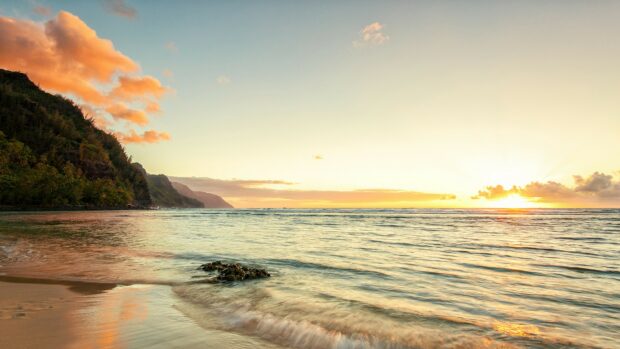 Kauai cliffside with sunset reflecting on ocean and sandy beach