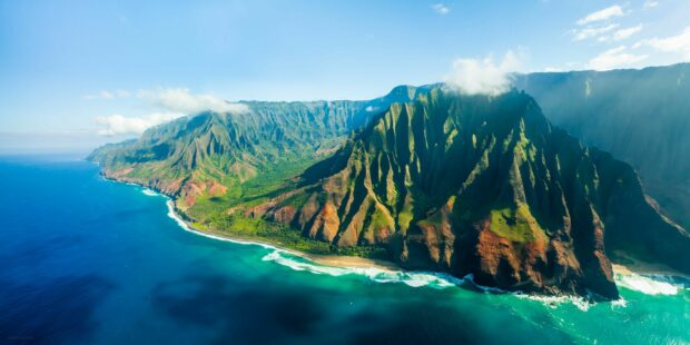 Dramatic Kauai cliffs with lush greenery and ocean coastline under blue sky