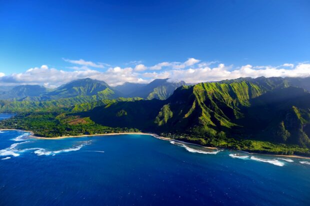 A vibrant Kauai landscape with lush green mountains and a deep blue ocean under a clear sky