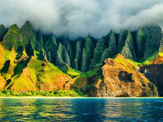 Lush Kauai cliffs covered in greenery under a cloudy sky near the ocean