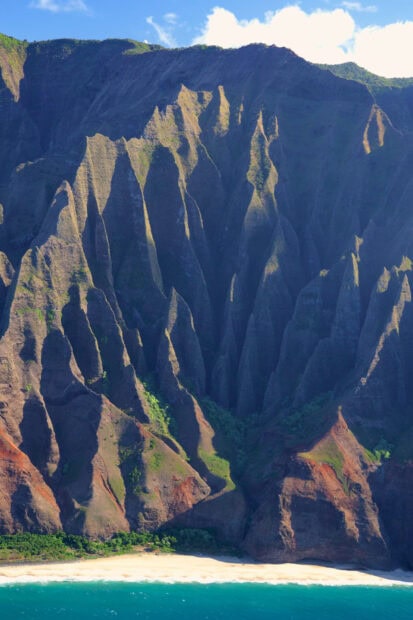 Steep cliffs of Kauai towering over a sandy beach with clear blue ocean waters