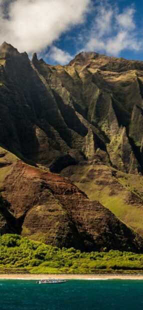 Steep Kauai mountain ridges with lush greenery and a boat near the shore