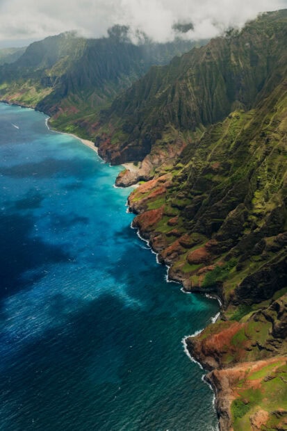 Aerial view of Kauai coastline with lush cliffs and clear blue ocean