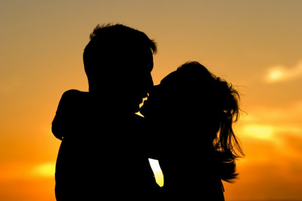 Silhouette of couple sharing a romantic kiss during sunset in a warm scenic view
