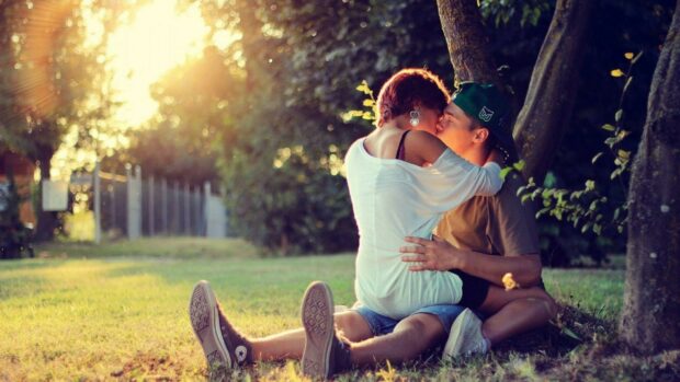 A couple sharing a tender kiss while sitting on the grass in a sunlit park