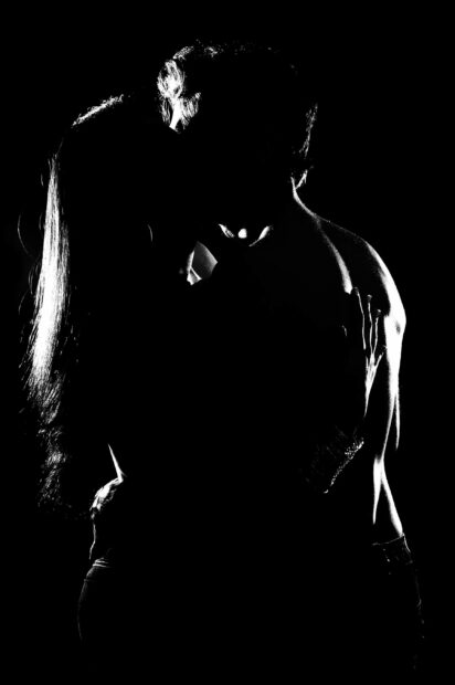 A romantic kiss between a man and a woman in silhouette light on black background