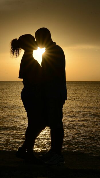 Couple sharing a romantic kiss by the sea during sunset with sun rays shining through