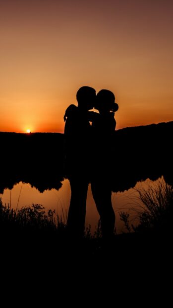 Silhouette of a couple sharing a romantic kiss at sunset over the lake