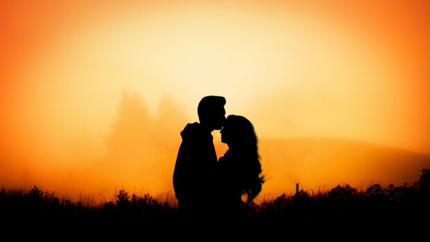 A couple sharing a tender kiss at sunset with a warm glowing sky in the background