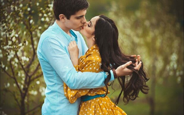 A couple sharing a gentle kiss in a garden surrounded by blooming flowers