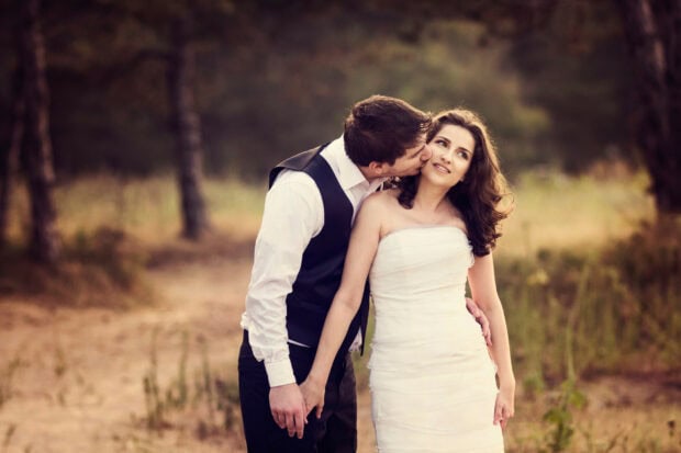 Groom giving a romantic kiss to bride in wedding dress outdoors in nature