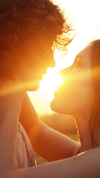 A romantic kiss between a couple with sunlight shining in the background