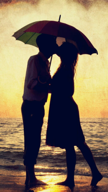 Couple sharing a kiss under umbrella at sunset by the ocean