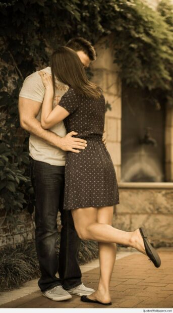 A couple sharing a romantic kiss outdoors with the woman lifting one leg in the air