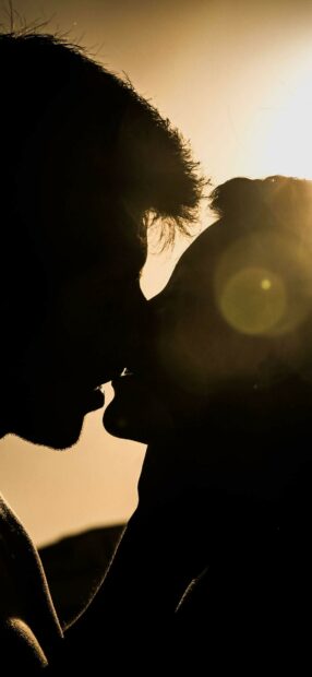 Couple sharing a romantic kiss in silhouette with sunset light in the background