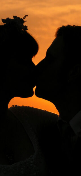 Silhouette of a couple sharing a romantic kiss at sunset with a flower in the woman's hair
