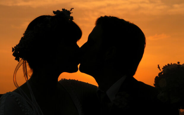 Silhouette of couple sharing a romantic kiss at sunset with flowers in hair and bouquet