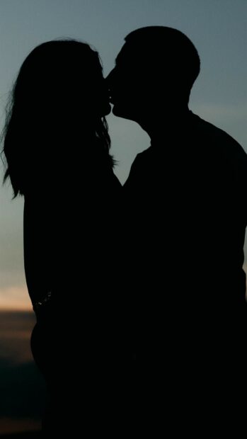 A silhouette of a couple sharing a kiss during sunset with a clear sky background