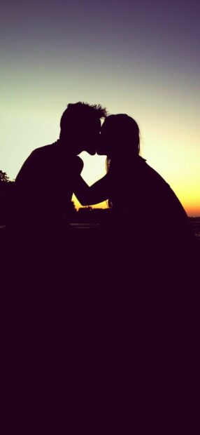 Couple share a romantic kiss at sunset with a beautiful sky background