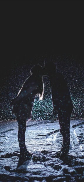 Couple sharing a kiss in the snow at night with snowflakes falling around them