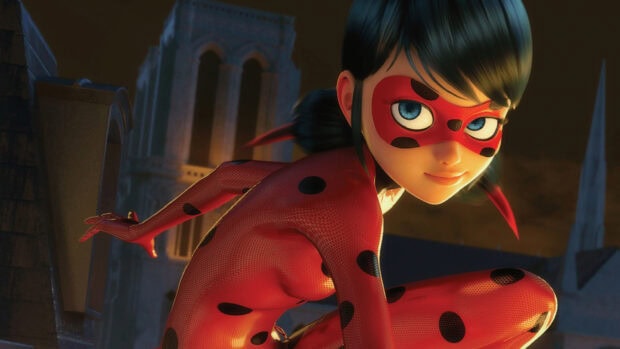 A close up of ladybug character wearing a red suit with black spots crouching on a rooftop at night