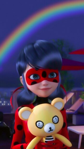 A ladybug character holding a yellow teddy bear under a rainbow at night