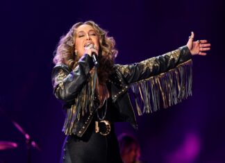 Lainey Wilson wearing a fringed leather jacket performing passionately on stage