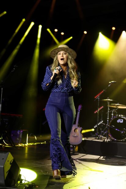 Lainey Wilson performing on stage wearing a hat and blue outfit