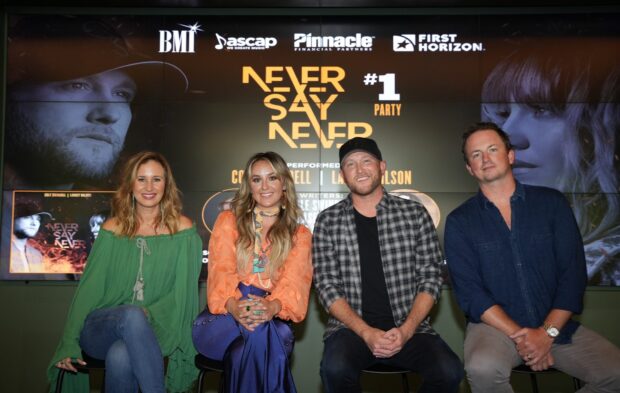 Lainey Wilson sitting with three people in front of a Never Say Never party promotional screen