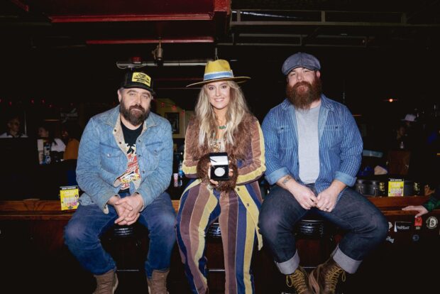 Lainey Wilson sitting with two men in a bar setting