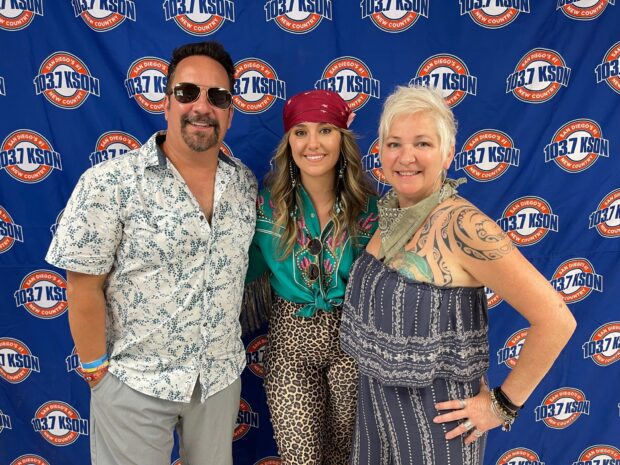 Lainey Wilson standing between two people at a 103.7 KSON event