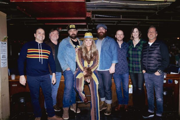 Lainey Wilson standing with a group of people wearing casual outfits indoors