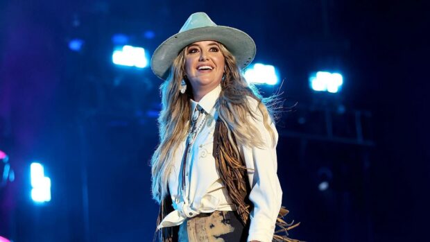 Lainey Wilson wearing a hat and western attire on stage during a live performance