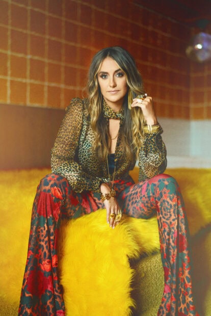 Lainey Wilson wearing patterned clothes sitting on a yellow fur couch in a stylish room